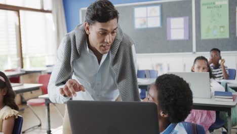 Feliz-Y-Diverso-Maestro-Hablando-Con-Un-Niño-Usando-Una-Computadora-Portátil-En-La-Clase-De-Escuela-Primaria,-Cámara-Lenta