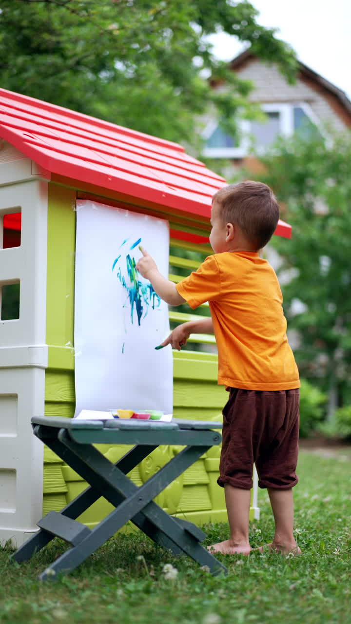 Painting with fingers in the garden. Adorable four-year-old toddler painting picture with his fingers. Vertical video.
