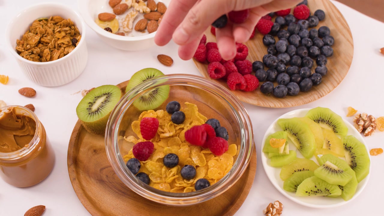 Ripresa dall'alto di una mano che mette lamponi e mirtilli in una ciotola di cereali con frutta fresca
