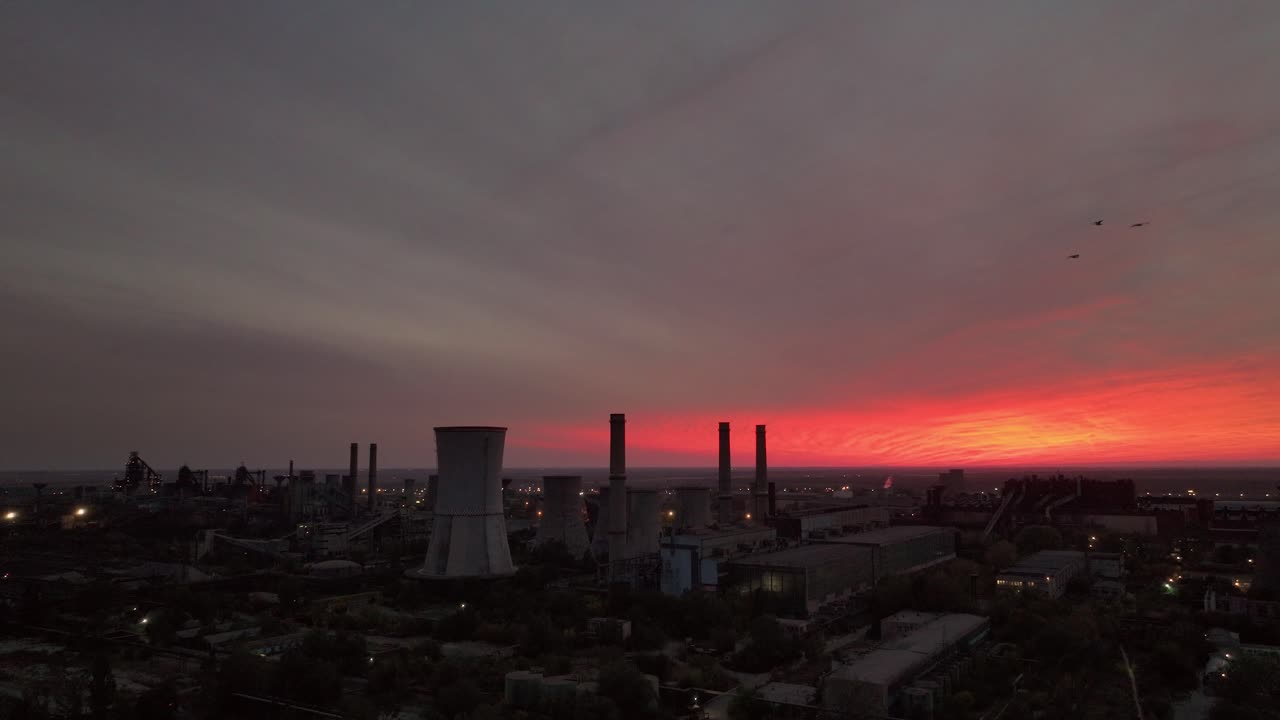 disparo de seguimiento de drones que muestra chimeneas contra una vibrante puesta de sol naranja nublada, que ofrece un impresionante paisaje industrial