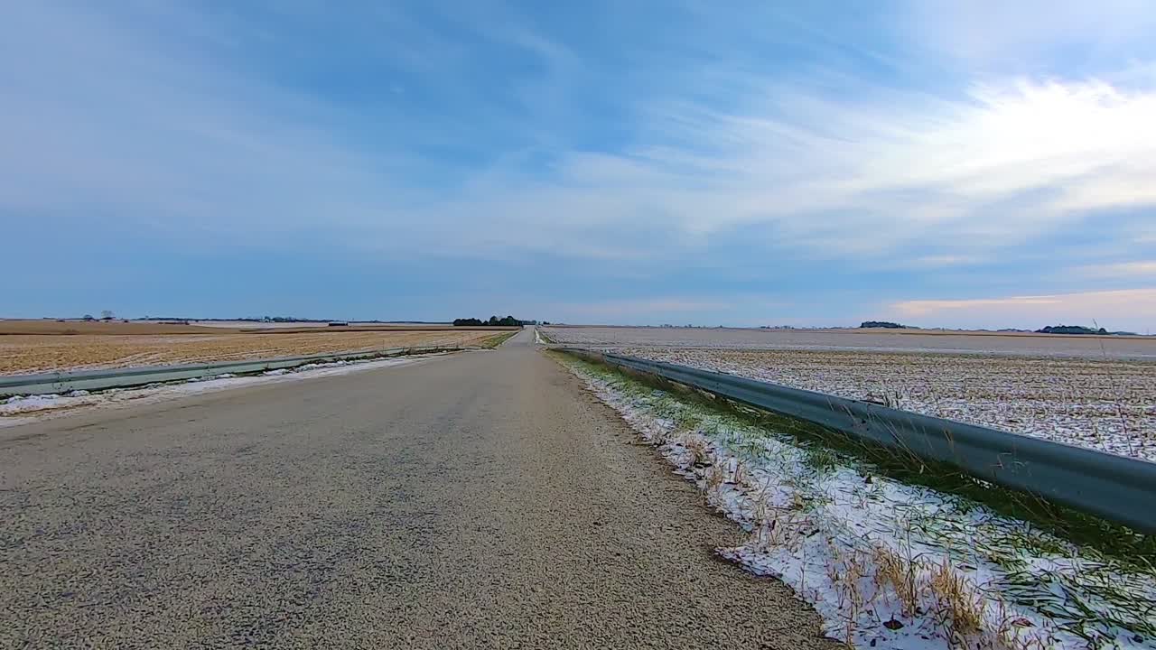 맑은 겨울 오후에 다리 위의 시골 길과 지나간 빈 들판을 운전하는 동안 뒷 창문을 통해 pov