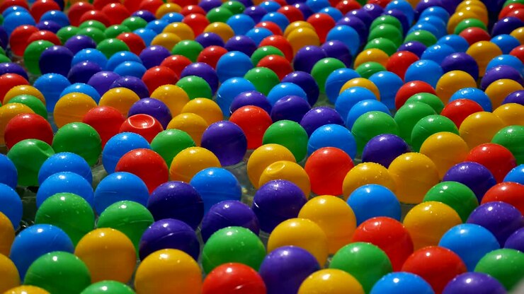 Colorful small plastic balls floating and moving in water, closeup view.