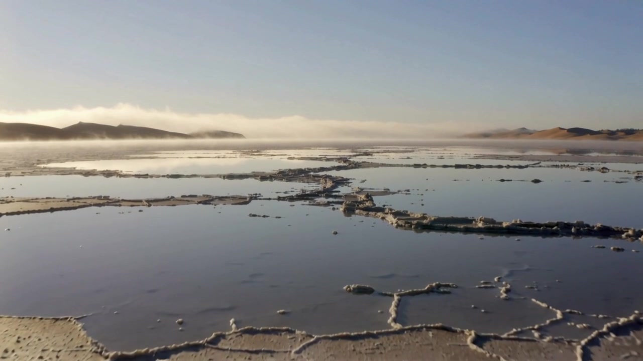 Starting cam forward, pushing low over salt flat, revealing mirror pools, white rims, horizon fog