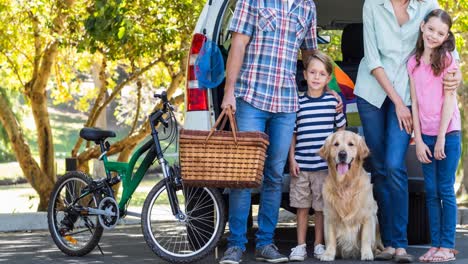 Happy-caucasian-parents,-son-and-daughter-standing-by-car-with-golden-retriever-pet-dog-in-park