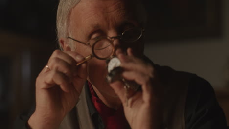 older passionate man evaluates an old silver skull watch in his office at night