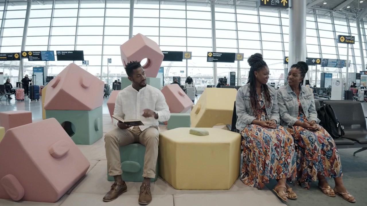 Uma Área de Lazer Colorida no Aeroporto: Pessoas relaxando entre blocos de construção gigantes e assentos confortáveis em um espaço lounge moderno.