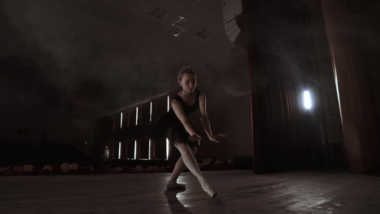 Young professional ballerina making circular movements on stage. Beautiful girl dancing in spotlights in evening during dress rehearsal.