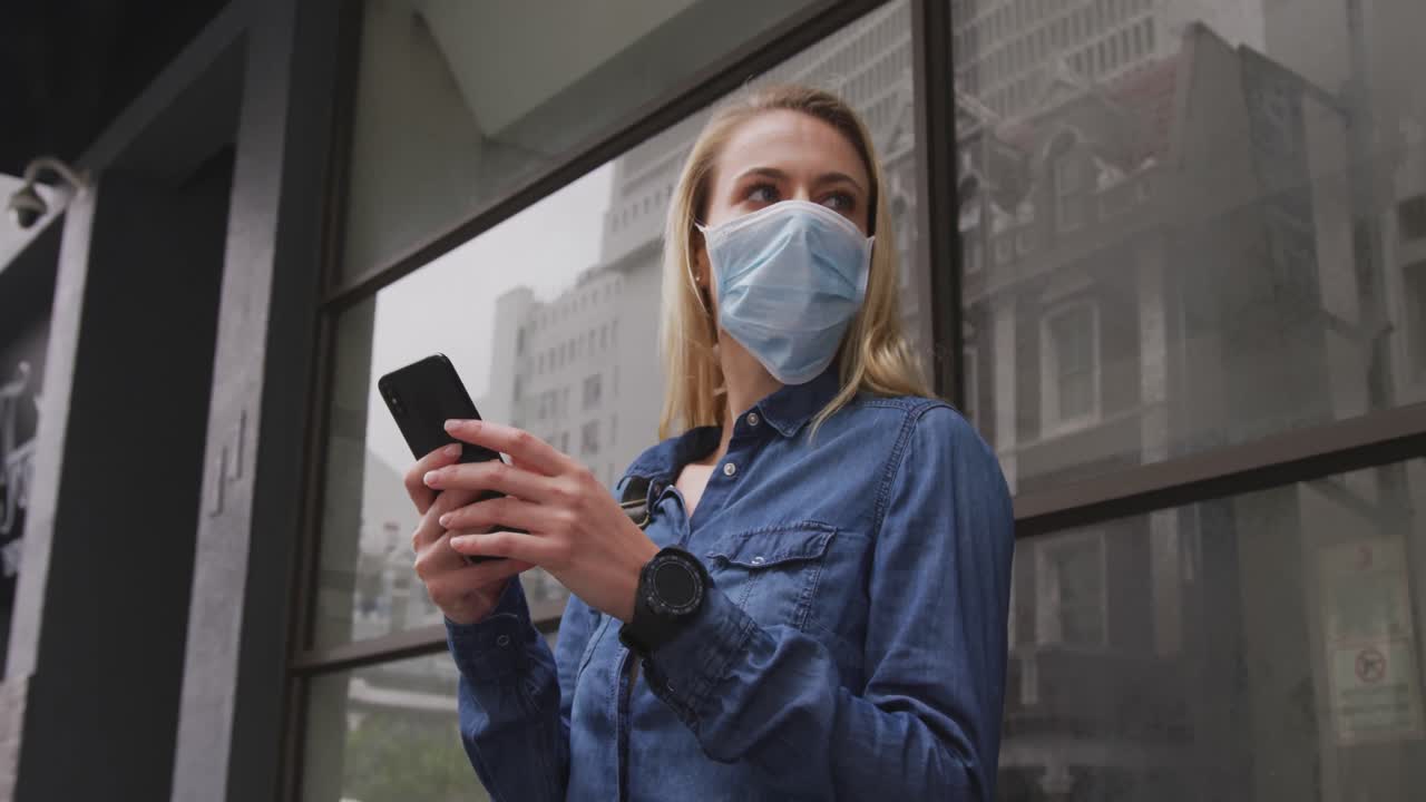 vista de ángulo bajo de una mujer caucásica con una máscara de coronavirus covid19 y usando su teléfono