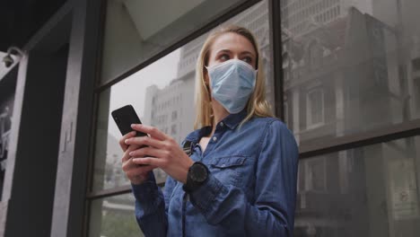 Low-angle-view-of-Caucasian-woman-wearing-a-coronavirus-Covid19-mask-and-using-her-phone