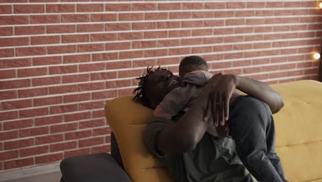 Afro-american-dad-with-his-son-hugging,-cuddling-together-at-home