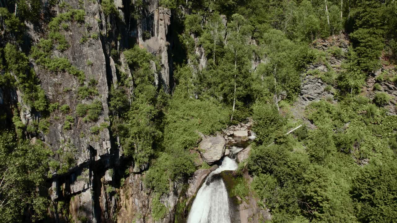 Vista aerea della Cascata Korbu che scorre in una gola rocciosa circondata da una fitta foresta verde nella Repubblica dell'Altai, Russia, un suggestivo paesaggio selvaggio in estate.