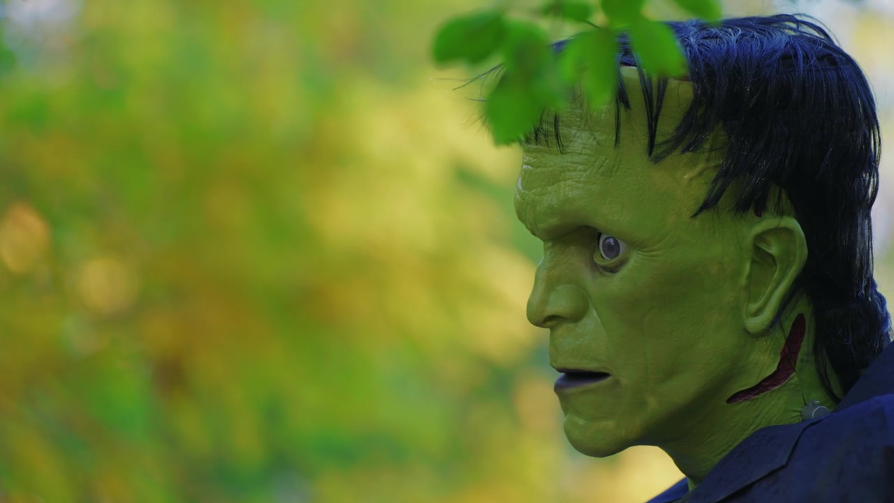 Close-up of Frankenstein's monster prop with vivid green skin and stitched neck, set against blurred foliage.