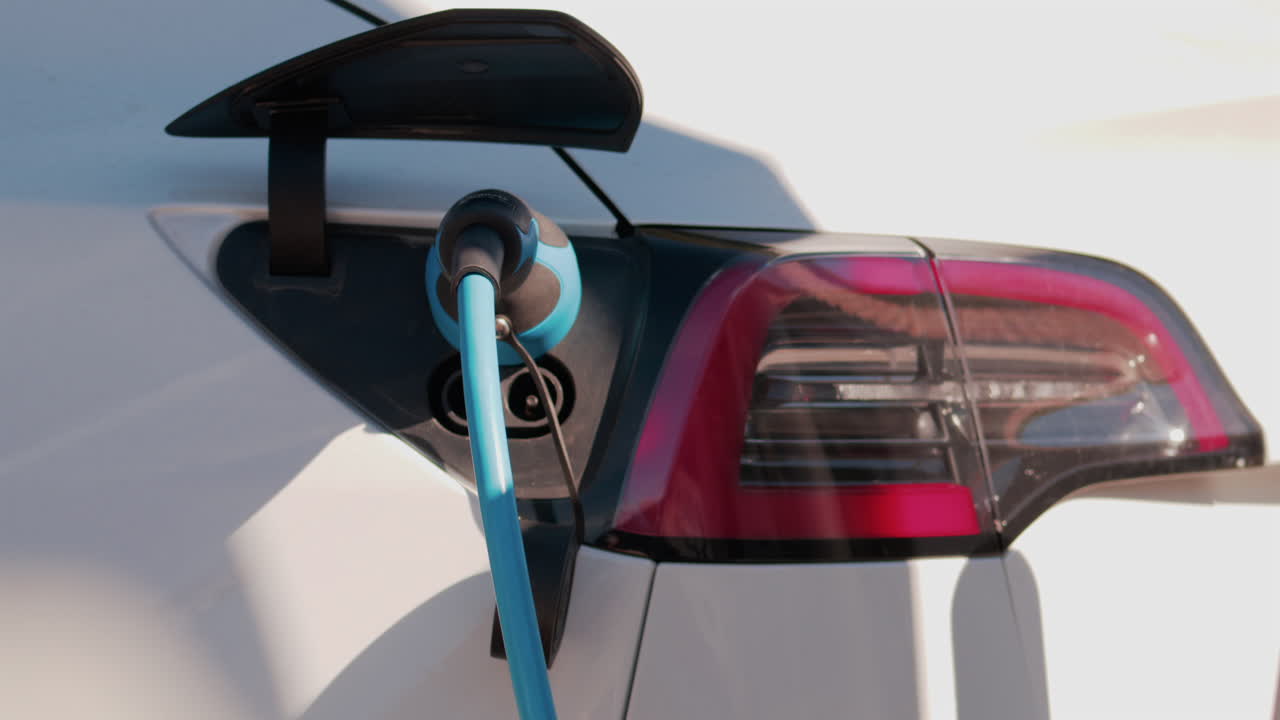 Close up of an electric car plugged into a blue charging cable in daylight