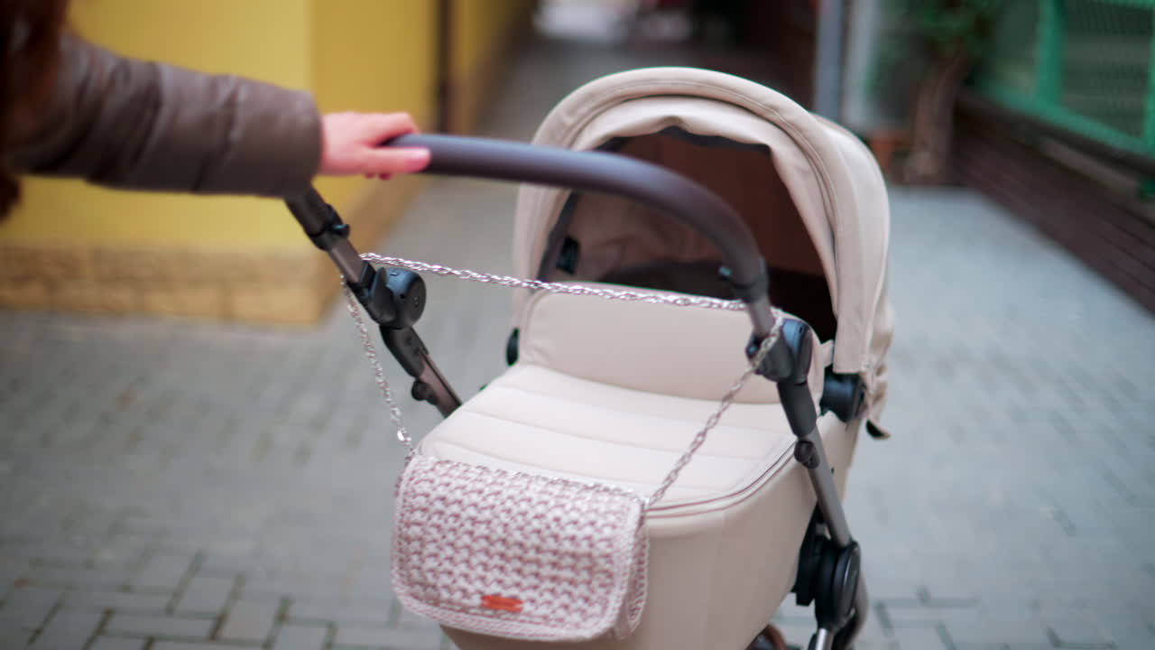 Close up of a hand pushing a beige baby stroller while walking through a colorful urban street