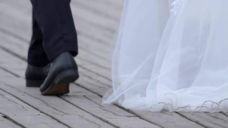 a man in a black suit and shoes is walking on the pier beside his bride to be