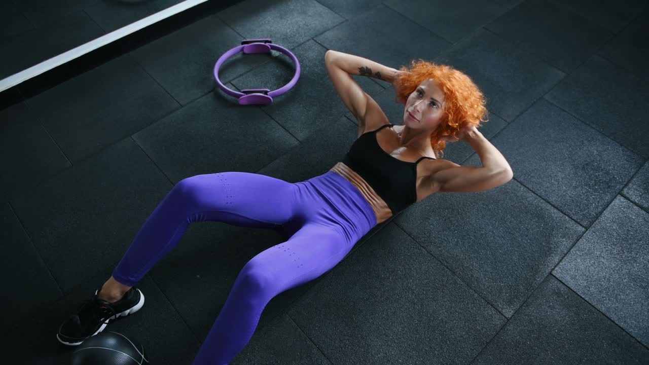 vista superior de una chica pelirroja deportiva con tipo de cuerpo musculoso haciendo abdominales en el gimnasio