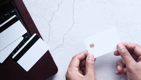 hands holding blank credit cards and a laptop on a desk.