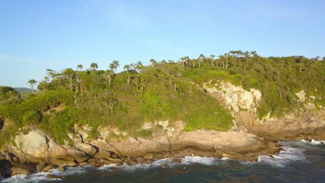 Aerial-shot-revealing-Bombinhas-town-behind-a-hill-with-vegetation-in-Brazil