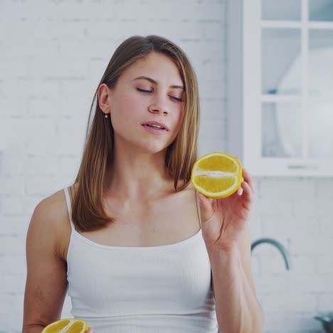 young woman with orange in cosy kitchen. healthy fruit in woman's hands indoors. beautiful female holding half of juicy orange. dieting concept.