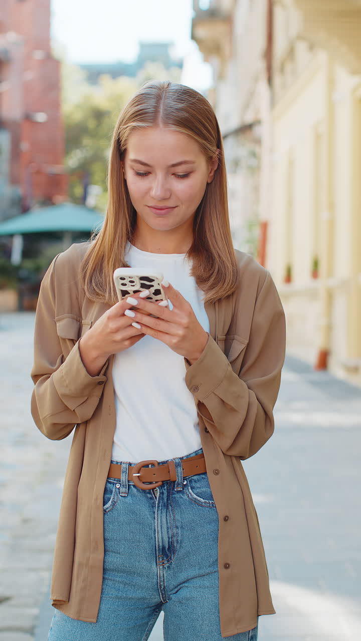 Beautiful young woman using smartphone typing text messages thinking and browsing internet on street