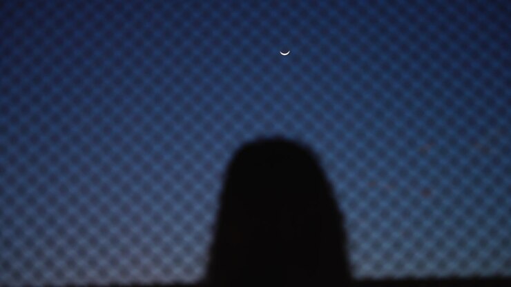 Unrecognizable woman looking at a crescent moon, with hands on a net