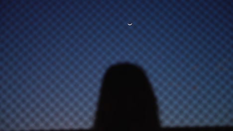 unrecognizable woman looking at a crescent moon, with hands on a net
