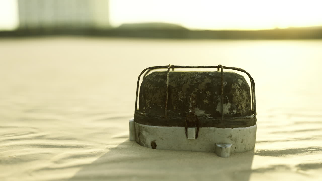 Old camping stove resting on sandy surface during sunset near urban setting