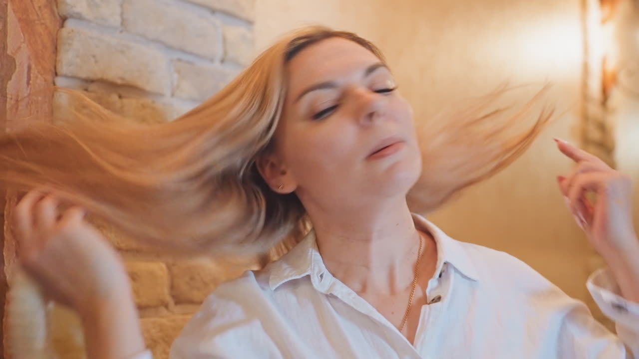 Mulher ajustando roupas tranquilamente por perto. Mulher relaxada ajustando suavemente o traje perto da parede texturizada. Mulher serena reposiciona delicadamente sua vestimenta de forma pacífica ao lado da superfície de tijolos texturizada.