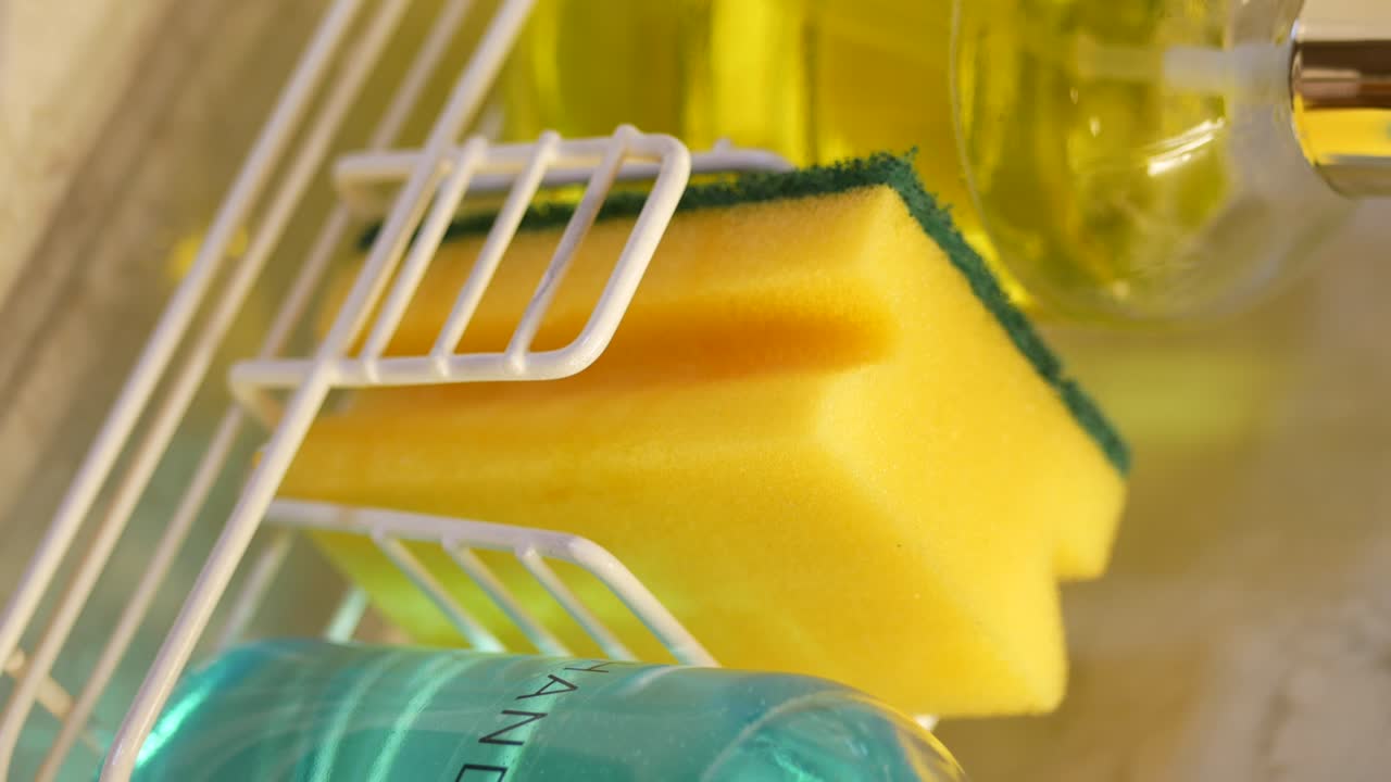 A close-up of a yellow cleaning sponge and blue liquid soap in a white dish caddy