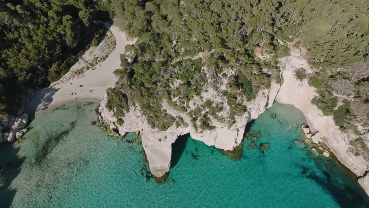 Luftfoto i fugleperspektiv af Mitjana-stranden på Menorca med stejle klippekanter langs vandrestien.