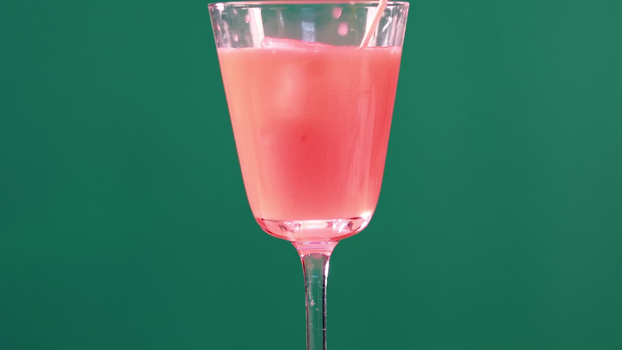 A pink beverage in a clear glass set against a vibrant green backdrop, showcasing simplicity and elegance.