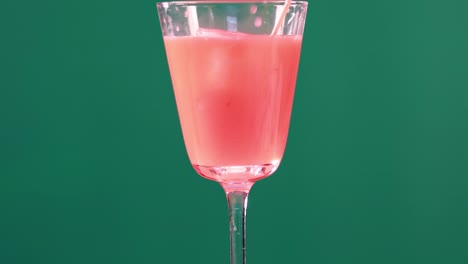 a pink beverage in a clear glass set against a vibrant green backdrop, showcasing simplicity and elegance.