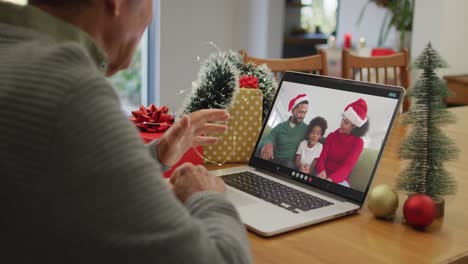 Kaukasischer-älterer-Mann,-Der-Einen-Weihnachtsvideoanruf-Auf-Dem-Laptop-Mit-Einer-Afroamerikanischen-Familie-Auf-Dem-Bildschirm-Führt