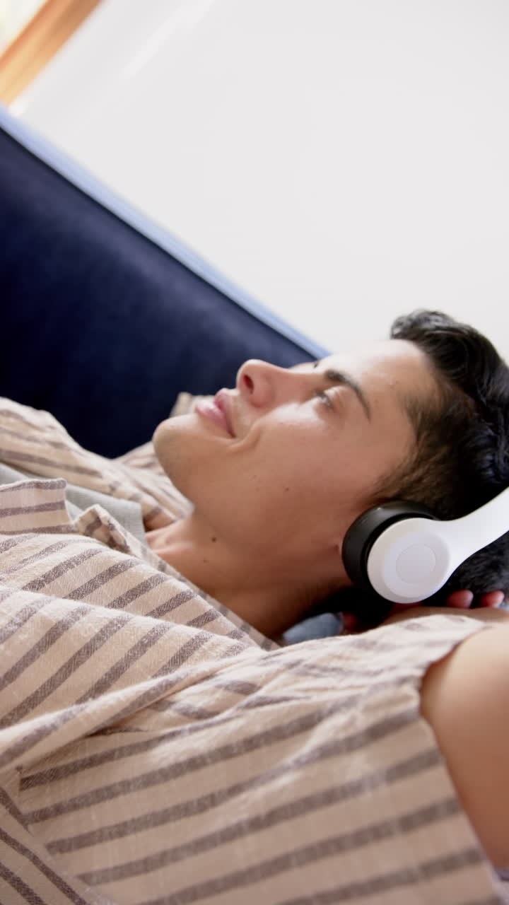 Vertical video of biracial man in headphones lying on couch, slow motion