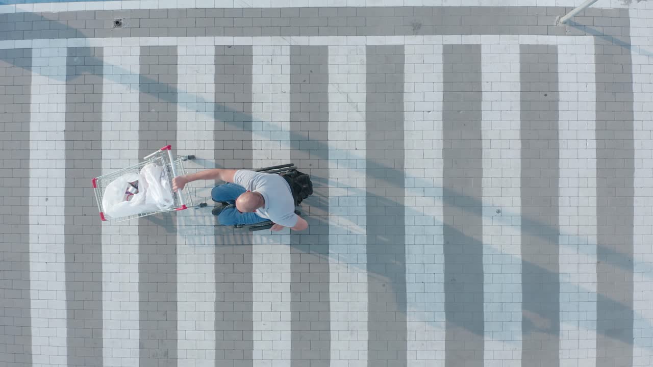 체어 에 앉은 장애인 이 슈퍼마켓 주차장 에서 자기 앞 에 바구니 를 밀고 있다