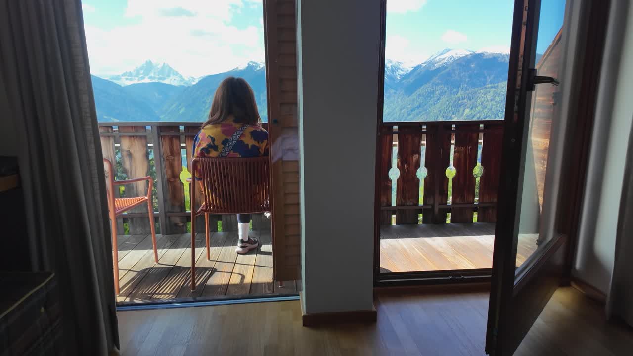 A slow-motion video of a girl admiring the morning view from an accommodation in the Italian Dolomites, with mountain peaks