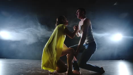 A-man-and-a-woman-dance-together-a-funny-dance-in-jeans-and-a-yellow-dress-on-stage-in-smoke.-Musical.