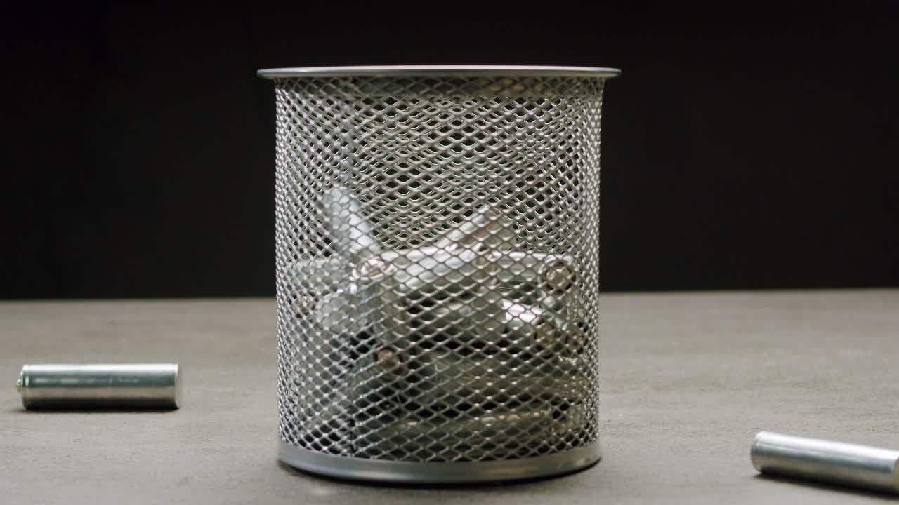 Silver batteries AA and AAA falling into wastebasket close-up. Double-A battery is a standard size single cell cylindrical dry battery. Batteries are common in portable electronic devices. Environmental impacts of lithium-ion batteries concept. An AA battery is composed of a single electrochemical c