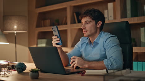 freelancer looking cellphone drinking coffee at work desk late evening close up.