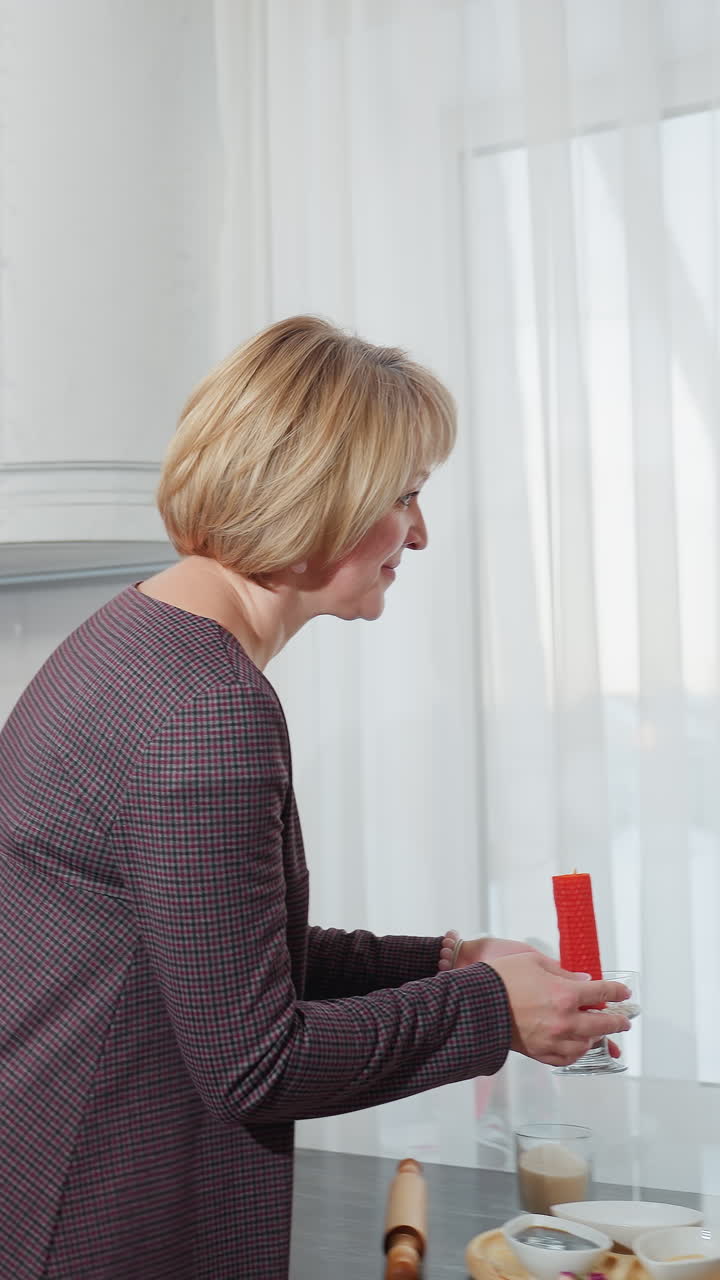 여성은 현대 부에서 은 불을 들고, 딸이 앉아서 읽는 테이블에 놓을 준비를 하고 있습니다. 부 장비와 장식은 밝은 자연 조명 속에서 쾌적한 가정 분위기를 만니다.