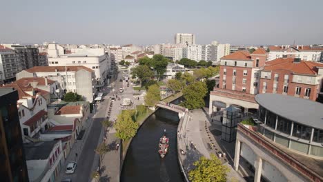 Aveiro-city-skyline-with-huge-tourist-canoe-sailing-through-downtown-canal,-aerial-view