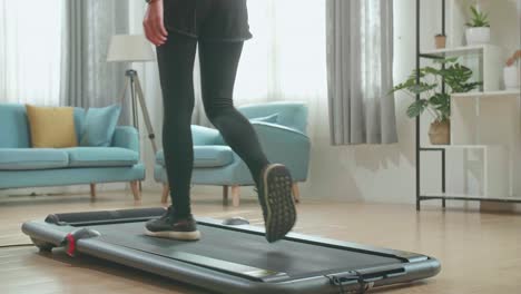 vista trasera de las piernas de una mujer asiática entrenando en una cinta de correr en casa