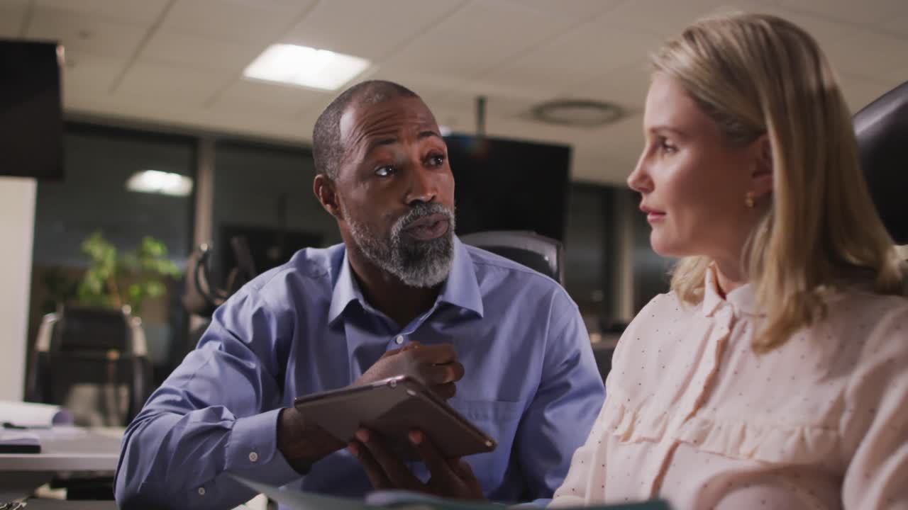 Professional businessman and businesswoman discussing over a digital tablet in modern office in slow