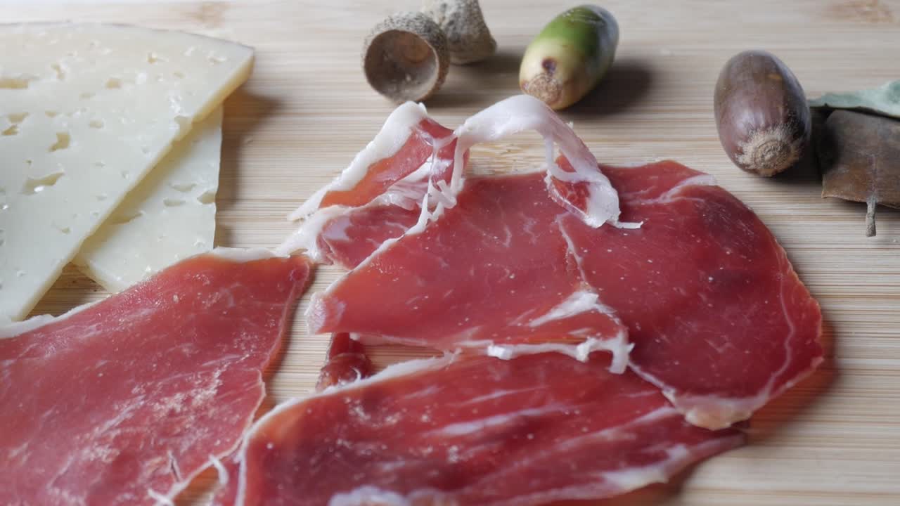 Slices of cured ham and cheese on a wooden board with acorns, rustic and appetizing