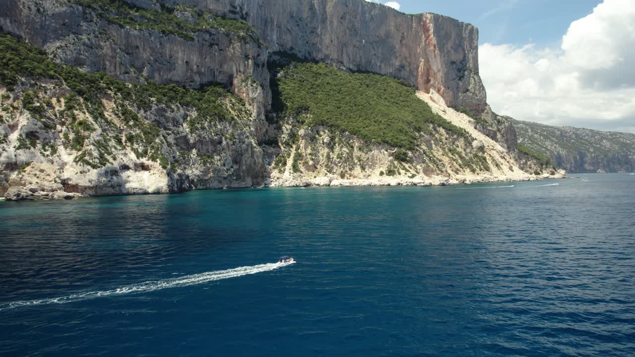 un barco se desliza en el mar azul debajo de altos acantilados en un día soleado con nubes por encima