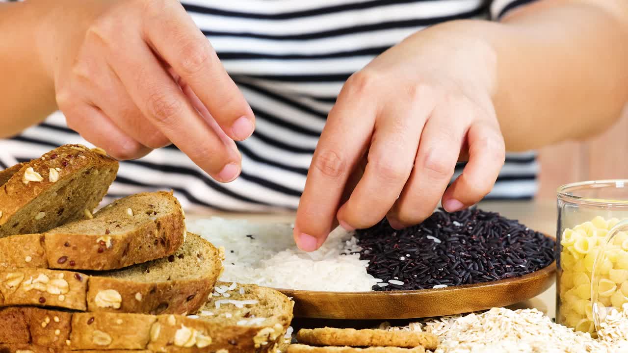 Hands sorting black rice and bread slices on a wooden board. Bright lighting enhances the detailed textures and colors