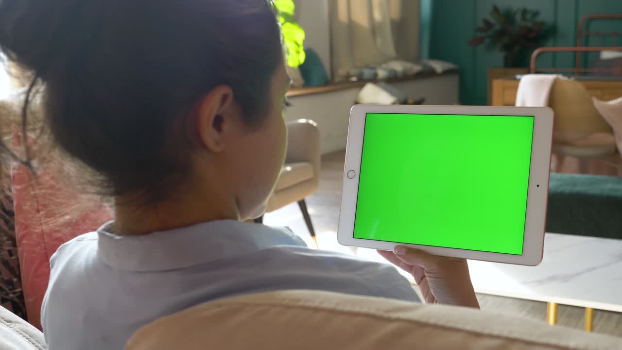 A Young Indian Woman Lying on Sofa in Living Room and Holding Tablet with Green Screen. Woman Use Tablet on Social Networks or to Shop Online.