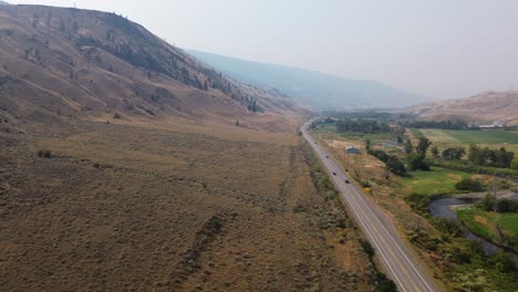 Aerial-Drone-Captures-Scenic-Landscape-Panning-Across-Hillside-Mound,-Cariboo-Highway,-and-River-in-BC,-Canada