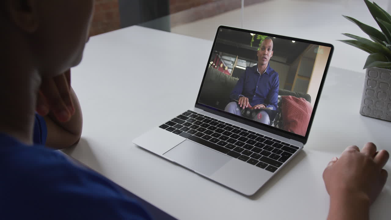 African american businesswoman sitting at desk using laptop having video call with male colleague