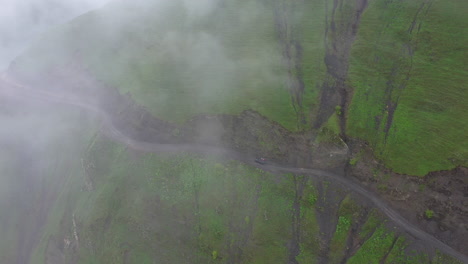 tiro de ángulo descendente de un vehículo que conduce al borde de un acantilado en el camino a tusheti pasando a través de las nubes, uno de los caminos más peligrosos del mundo